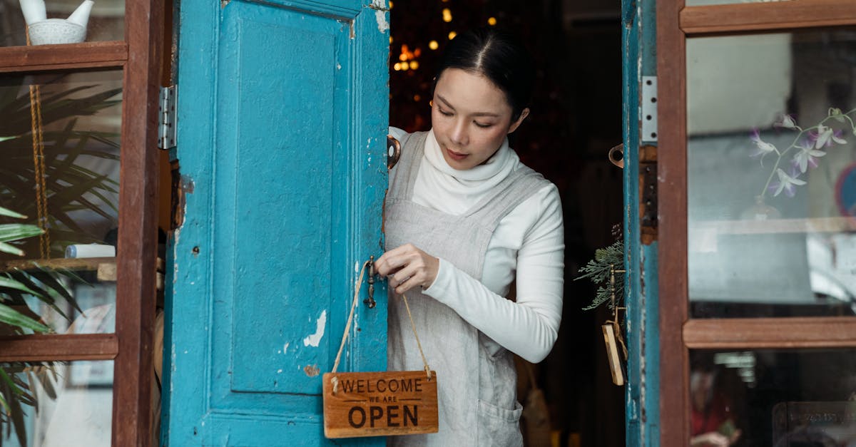 A woman adjusts an open sign on a blue wooden door of a cafe inviting customers inside.