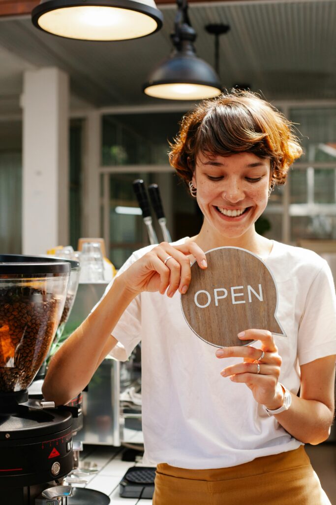 Happy barista holding open sign in a cozy café, ready to welcome customers.