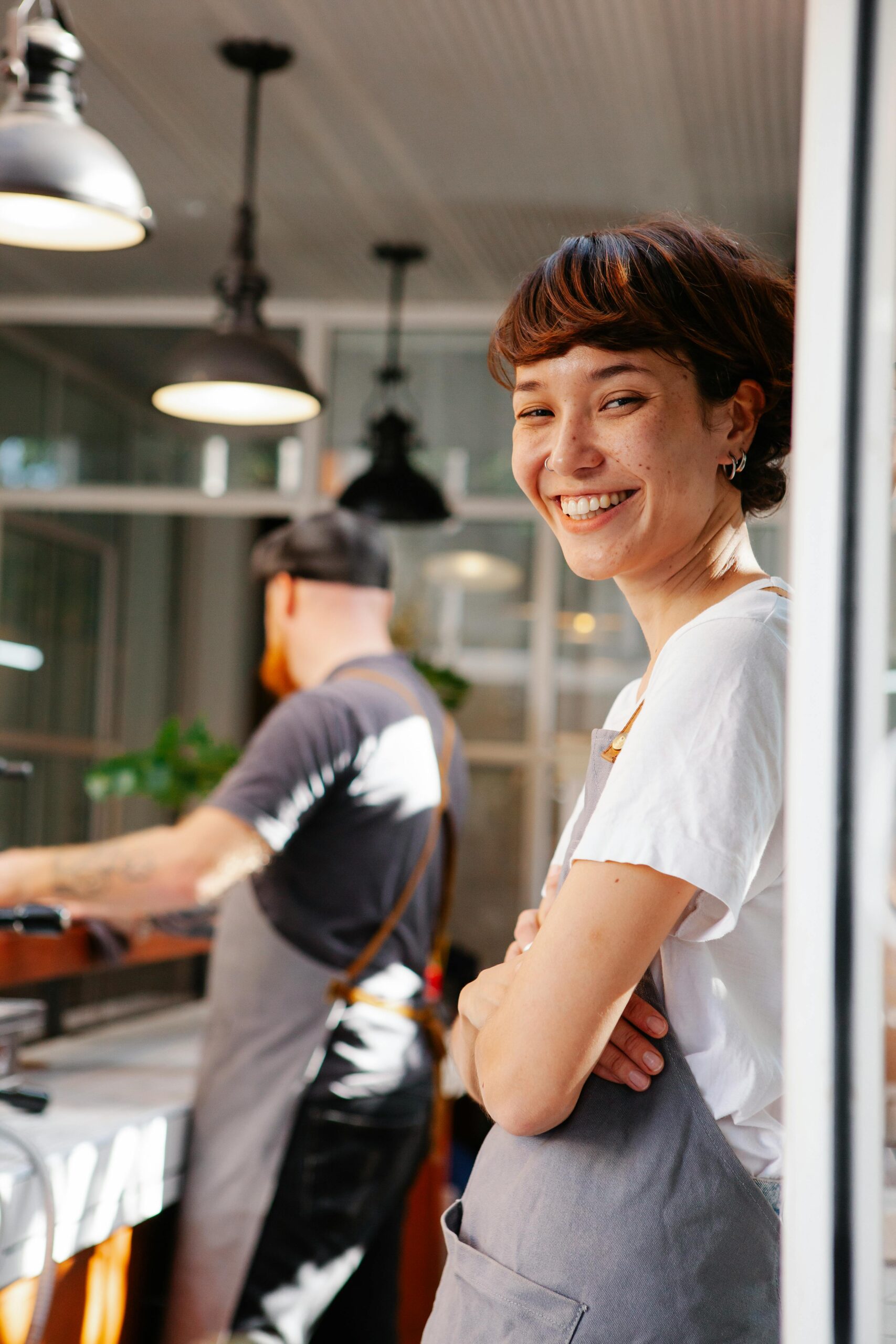 A cheerful barista smiling brightly in a modern cafe setting, creating a welcoming atmosphere.