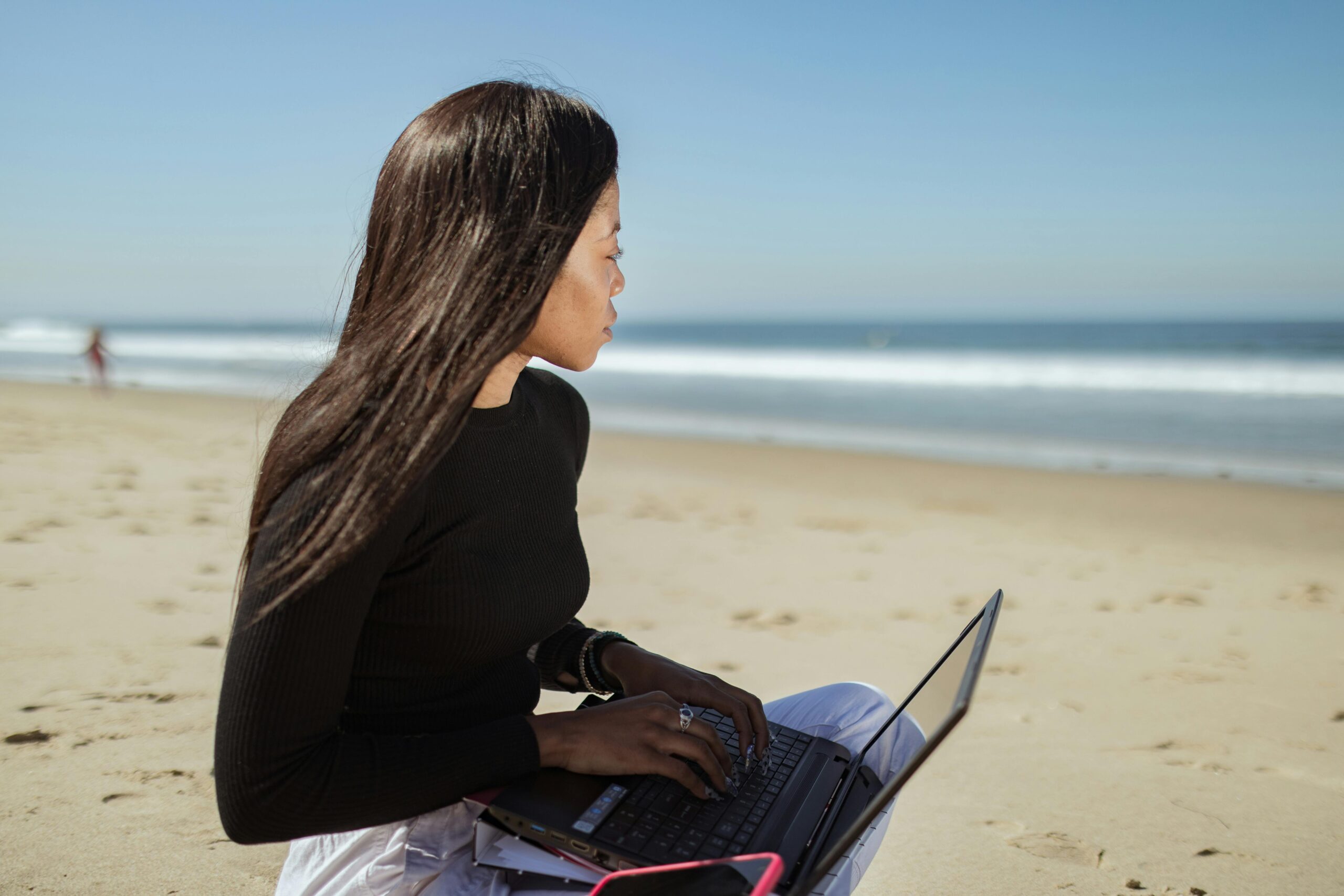 Woman working with a laptop on a sandy beach, enjoying a sunny day at the seaside.