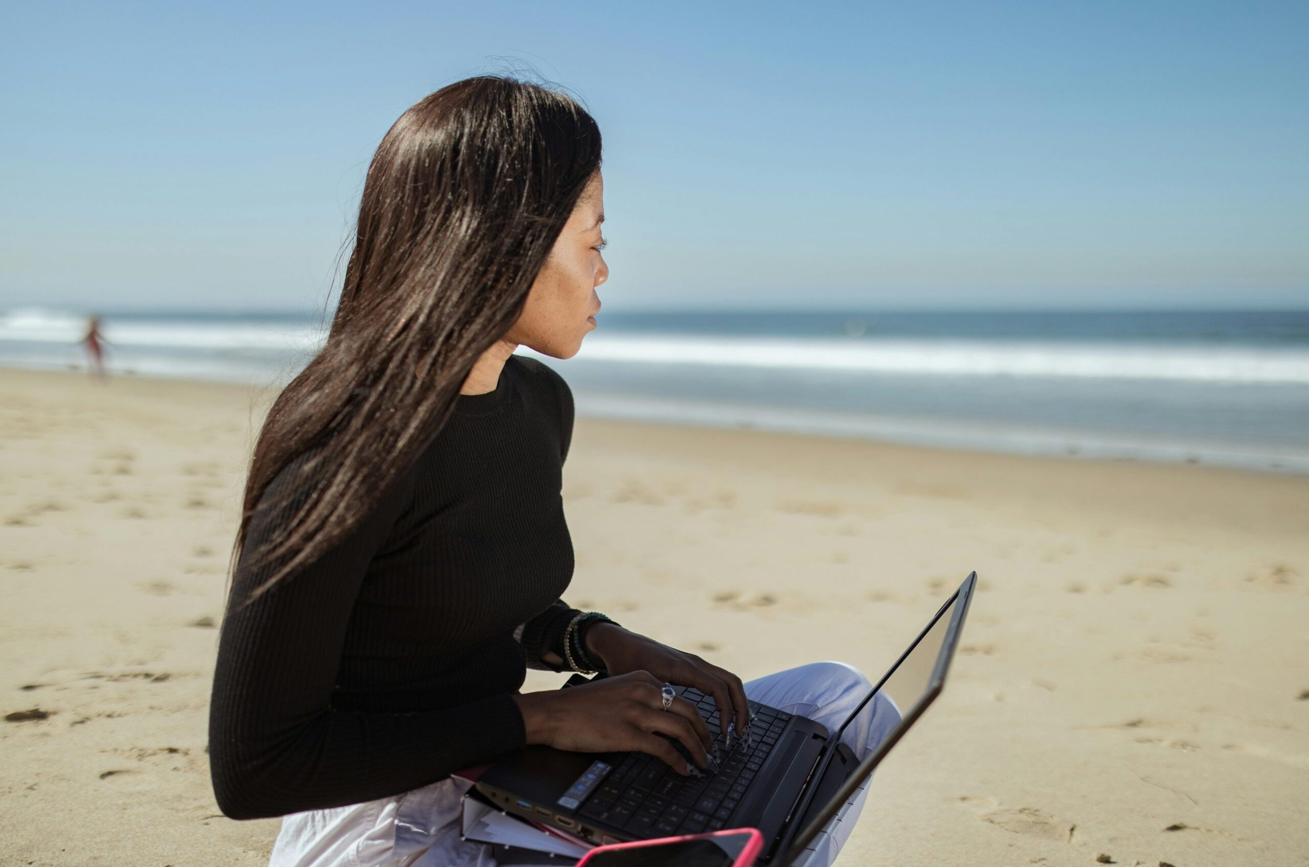 Woman working with a laptop on a sandy beach, enjoying a sunny day at the seaside.